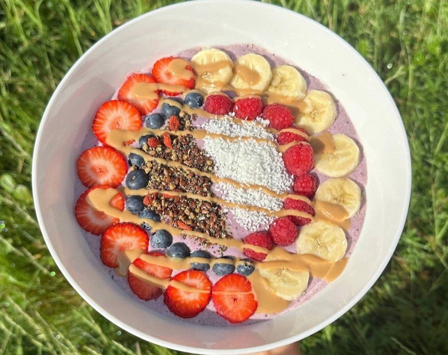 Purple smoothie bowl topped with strawberries, blueberries, raspberries, banana, coconut and peanut butter drizzle