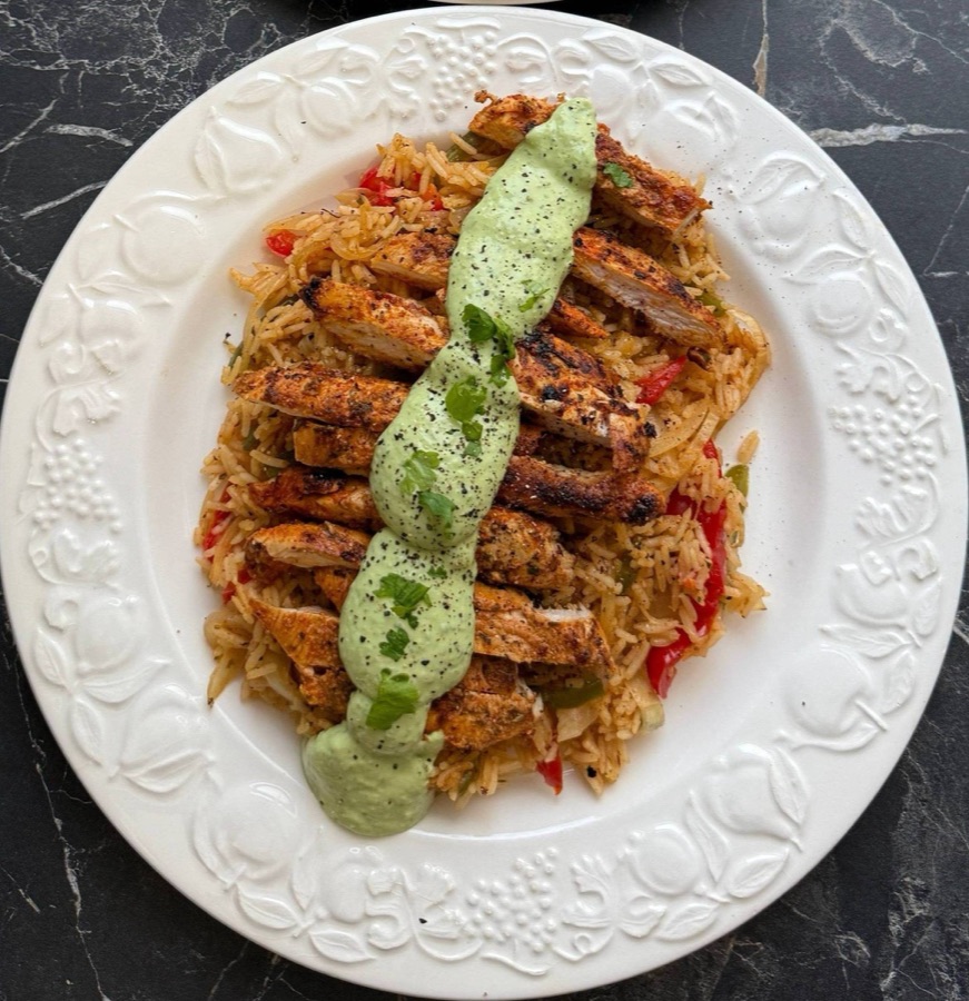 Sliced grilled chicken over seasoned rice with a green sauce on a white plate