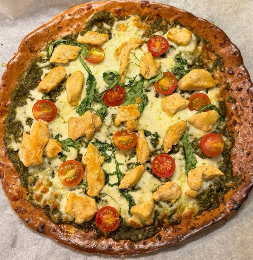 Pizza topped with pesto, melted mozzarella, chicken pieces, rocket and halved cherry tomatoes