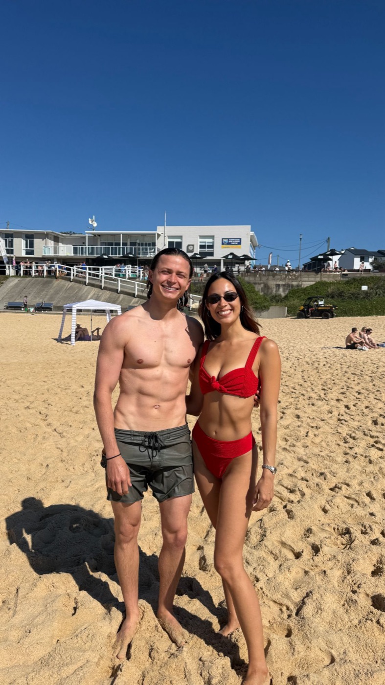 Aeran and Alexandra smiling together on a sunny beach under a clear blue sky