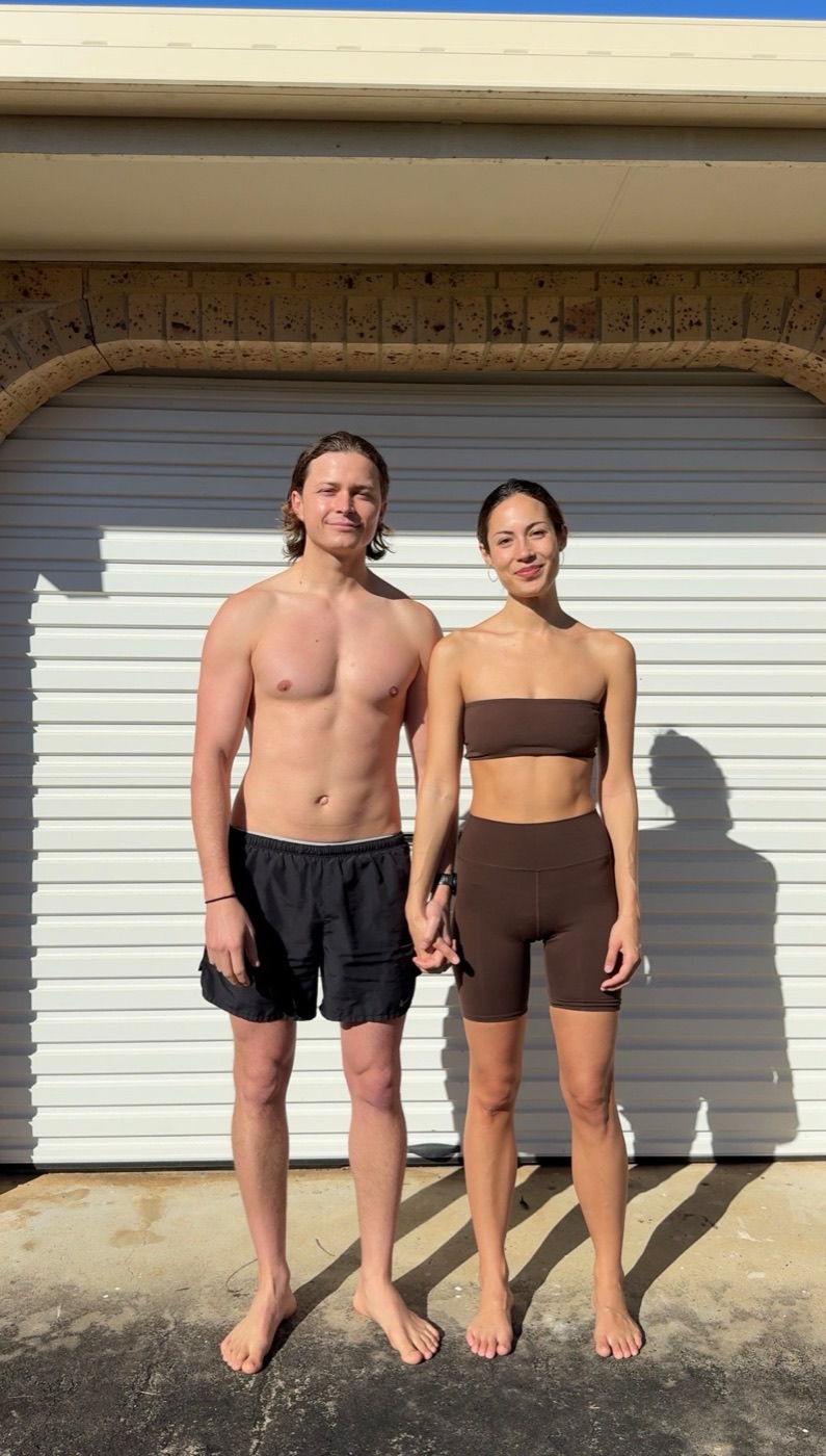 Before: Aeran and Alexandra standing hand in hand in front of a white garage door, at the start of their 50-day program
